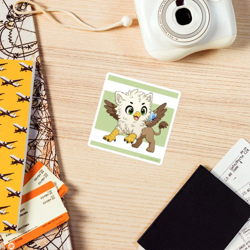 A product mockup of the 4x4" magnet featuring Echo the Griffin laying on a cluttered wooden desk
