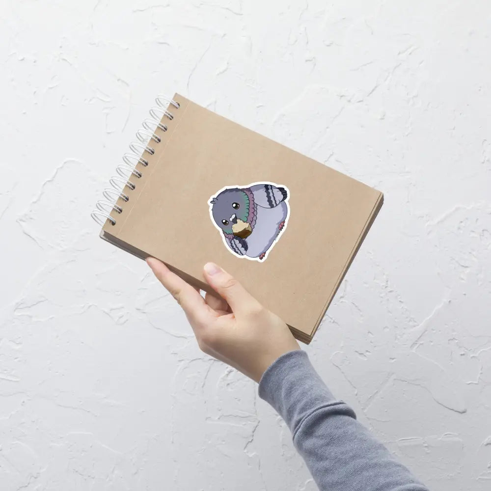 A product mockup of a 4x4" vinyl sticker on a brown notebook cover, featuring Fred the Pigeon.