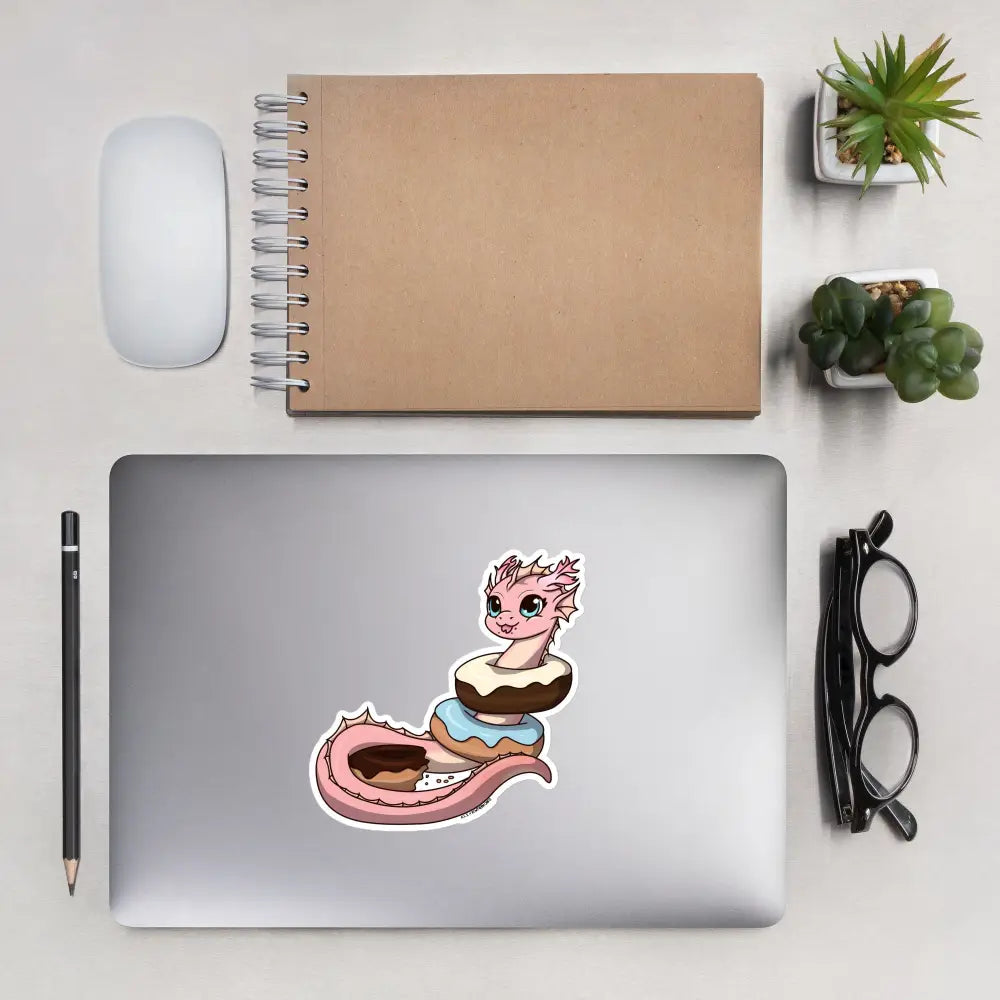A product mockup of a 5x5" vinyl sticker on a silver laptop lid, featuring Pearl the Coral Dragon.
