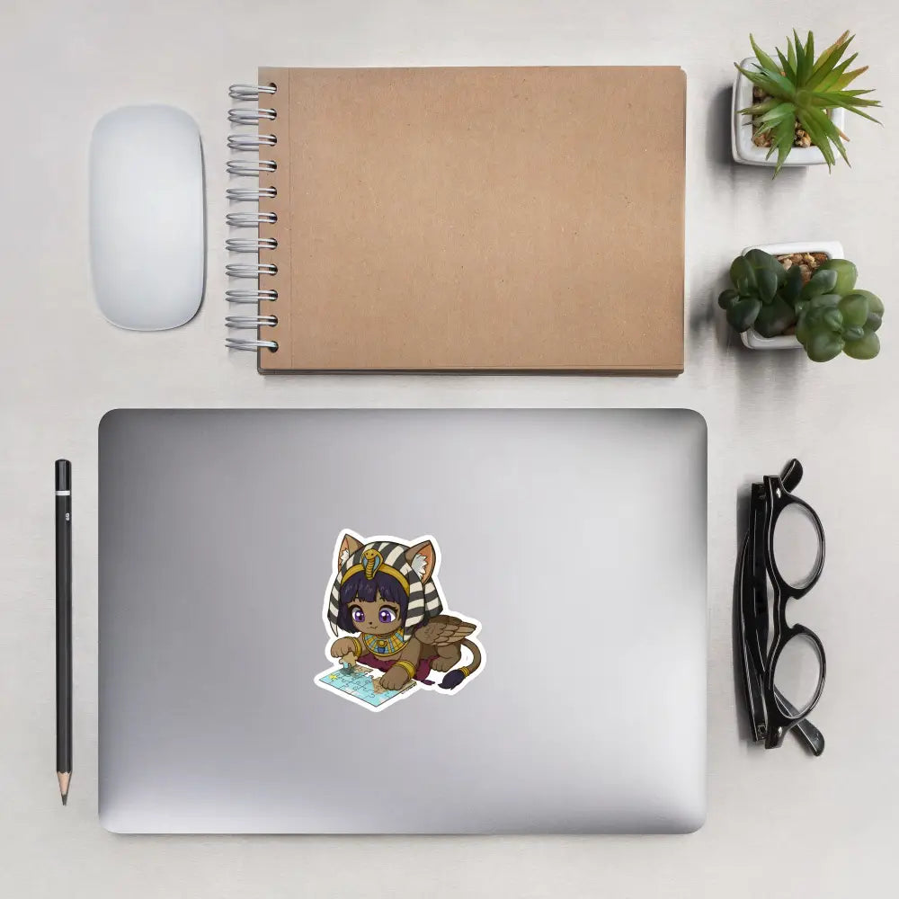 A product mockup of a 4x4" vinyl sticker on a silver laptop lid, featuring Safiya the Sphinx.