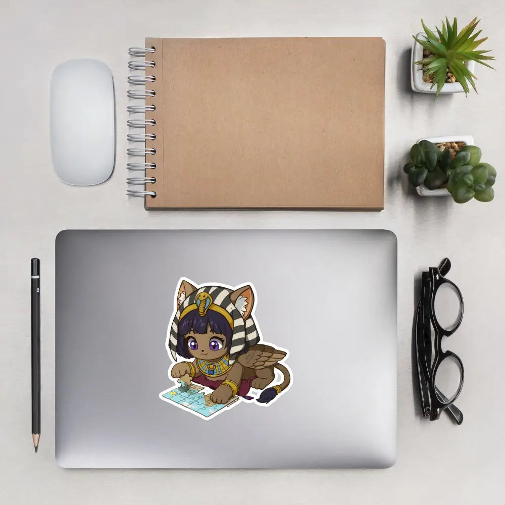A product mockup of a 5x5" vinyl sticker on a silver laptop lid, featuring Safiya the Sphinx.