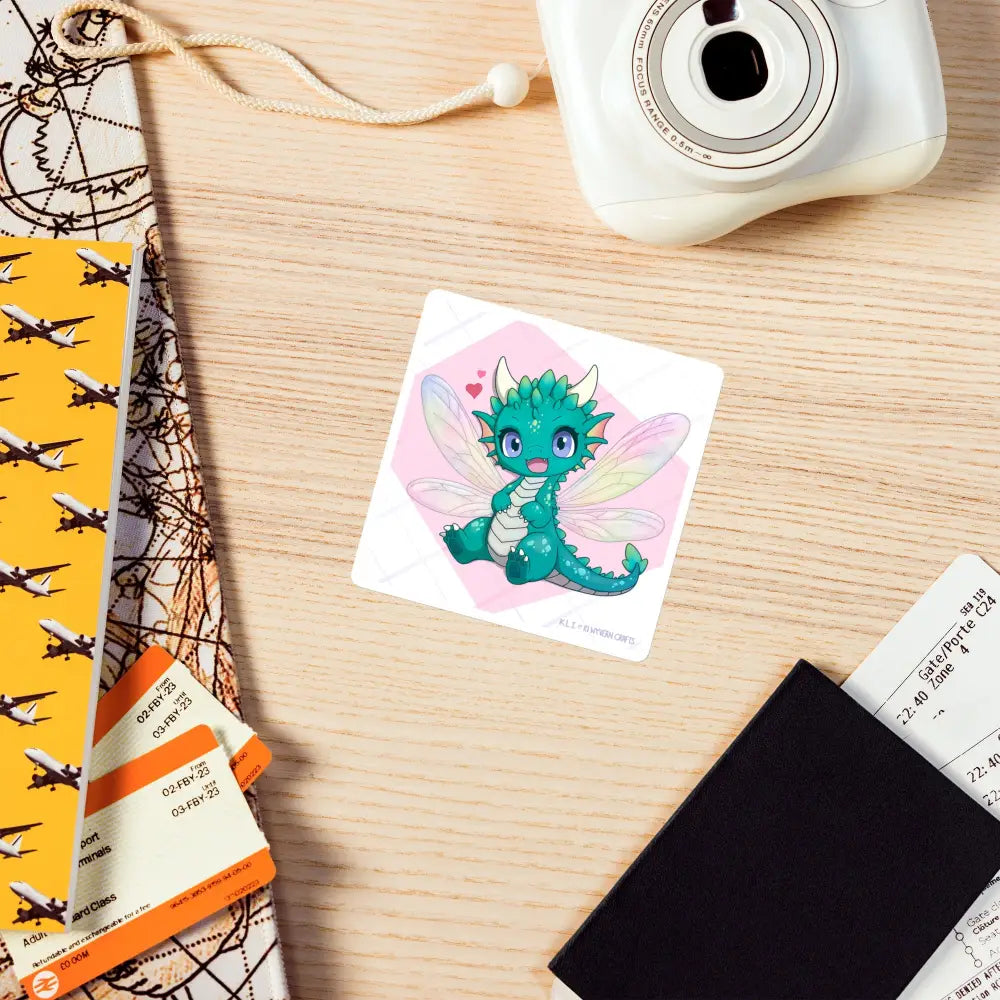 A product mockup of the 4x4" magnet featuring Tetra the Fairy Dragon laying on a cluttered wooden desk