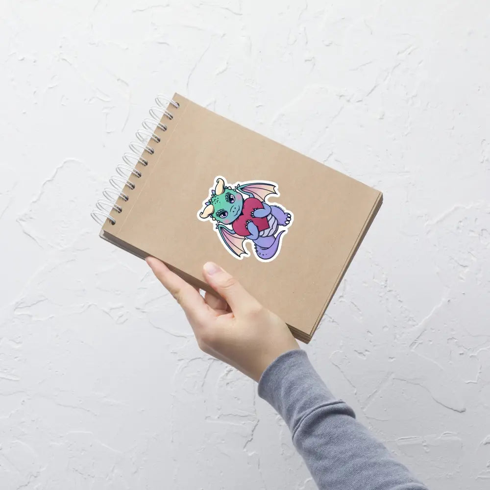 A product mockup of a 4x4" vinyl sticker on a brown notebook cover, featuring Vivian the Dragon.
